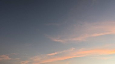 Altta pembe ve turuncu ince bulutların yumuşak bir gradyanı ile sakin bir gündoğumu gökyüzü, yukarıdaki derin mavilikte pürüzsüz bir şekilde harmanlanıyor. Görüntü huzurlu ve huzurlu bir atmosfer taşır..