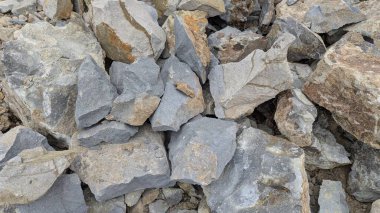 Mavi-gri-kırmızımsı-kahverengi tonlarının hakim olduğu, keskin kenarlı, parçalanmış kaya yığınının yakın çekimi. Engebeli dokusu tüm çerçeveyi dolduruyor..