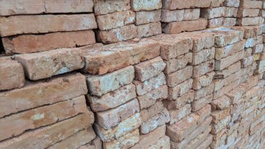 Sıkıca istiflenmiş yeni yapılmış kırmızı-turuncu tuğlaların pürüzlü kenar dokusunu gösteren detaylı bir yakın çekimi. Düzenleme tekrarlanan bir geometrik desen oluşturur.