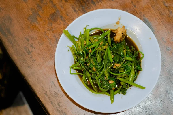 Bahasa Endonezya 'da beyaz tabağa yerleştirilmiş su ıspanağı veya cah kangkung düz çekim veya üst görünüm