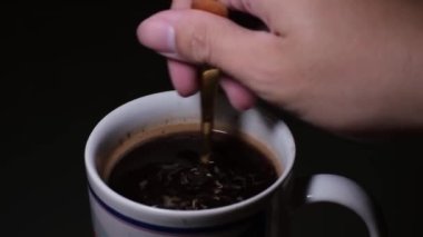 Bir el, bir fincan kahveyi karıştırırken yakın çekim.