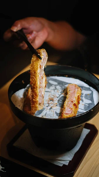Portrait or vertical high-angle photo of unfocused hand grilling beef katsu on a white barbecue grill mat using a black pan