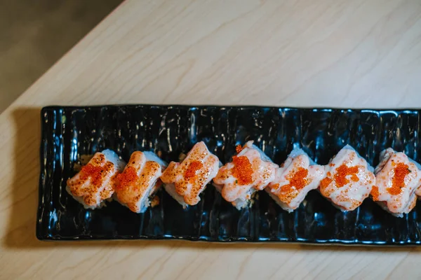 Tahta bir masanın üzerinde uzun siyah bir tabakta duran Tobiko suşi setinin düz uzanmış ya da üst görünüm fotoğrafı