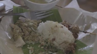 Yakından çekilen görüntülerde Balili Domuz Pirinci ya da Nasi Babi Guling paslanmaz çelikten yapılmış bir çatal ve kaşık kullanıyor.