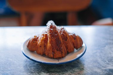 A croissant on a small white plate on a marble table with bokeh. Isolated.