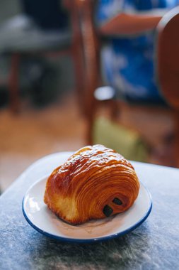 A chocolate croissant or pain au chocolat in a white small plate in a marble table with bokeh. Isolated. Portrait or vertical.