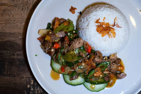 Stir-fried pork meat with Indonesian herbs and spices and white rice on a white plate. Flat lay or top view.