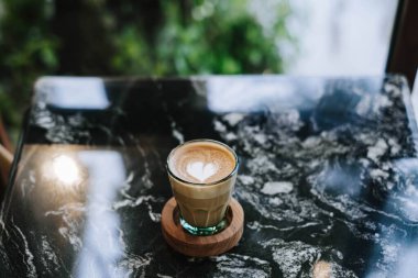 Minimalist Kahve Latte, tahta bardak altlığı ve Mermer Masa. Bulanık Arkaplan.