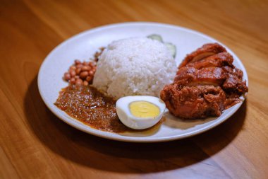 İçinde çıtır tavuk, yumurta, yer fıstığı, Lemak sosu ve bulanık arkaplanlı ançüez balığı bulunan bir tabak Nasi Lemak.