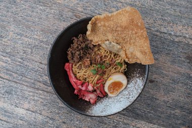 Dümdüz uzanmış ya da bir kase kızarmış Çin eriştesi dilimlenmiş tavuk, Char Siu, yarım haşlanmış yumurta ve ahşap masada kızarmış hamur köftesi.