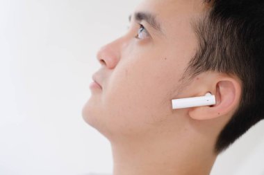 Genç bir Asyalı adamın kablosuz kulaklıkları dinlerken yüzünün bir kısmı yakın plan çekilmiş. Kulaklığa odaklan. Odaklanmamış ya da yüzeysel alan derinliği. İzole edilmiş beyaz arkaplan.