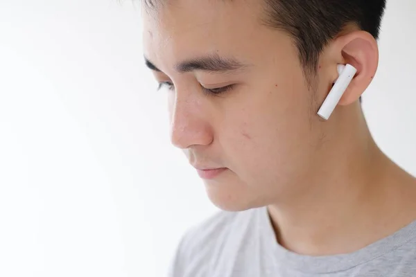 一个年轻的亚洲男人正在听白色的真正的无线立体声耳机 他的脸的特写和软聚焦镜头 孤立的白色背景 — 图库照片