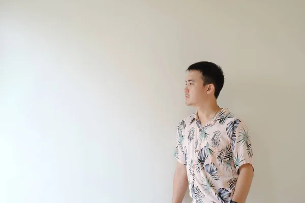 熱帯模様のピンクのシャツを着た若いアジアの男が立っていて カメラの右側か左側を見ている 隔離された白い背景 — ストック写真