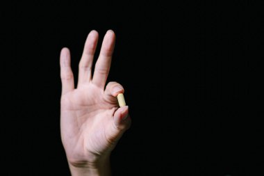 Sarı hap işaret ederek tutulur ve diğer üç parmağıyla başparmak havada durur. İzole edilmiş siyah arka plan. Reklam için uygun..