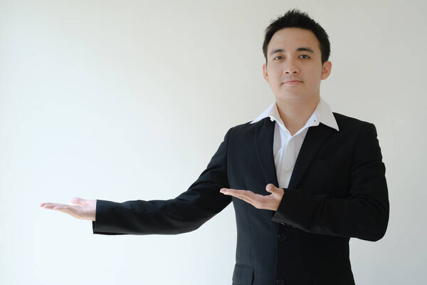 Young Asian businessman opens his both palm hands to his right side and looking to the camera. Isolated white background.
