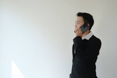 Beyaz gömlek ve siyah takım elbiseli genç bir Asyalı işadamı akıllı telefon kullanarak arıyor. İzole edilmiş beyaz arka plan. Reklam için uygun..