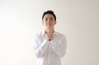 Beyaz tişörtlü genç Asyalı dua ediyor. İzole edilmiş beyaz arkaplan.