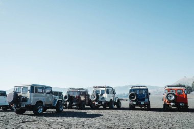 A lot of off-road vehicles or full-sized SUVs are parked in the desert of Bromo mountain national park area with a clear blue sky. Suitable for commercial use.