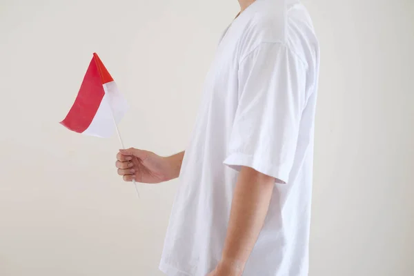 Beyaz tişört giyen bir adam, Bendera Endonezya ya da Endonezya bayrağını tutarken, sol tarafı da izole edilmiş beyaz arka planda tutuyor..