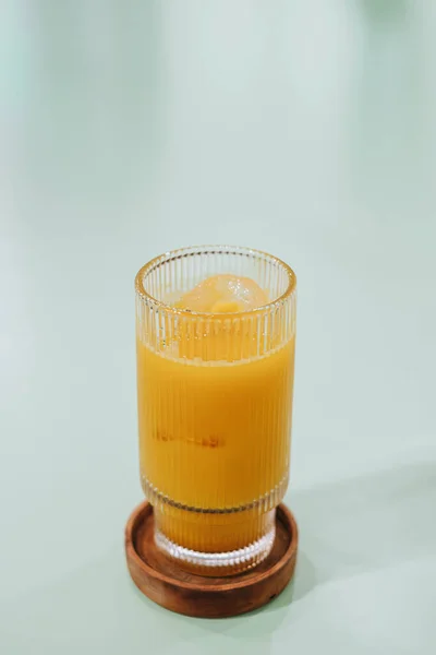 Bir bardak buzlu Kunir Asem 'in portresi ya da dikey ve seçici odak noktası izole edilmiş yeşil pastel masadaki geleneksel Java bitkisel ilaç içecekleri.