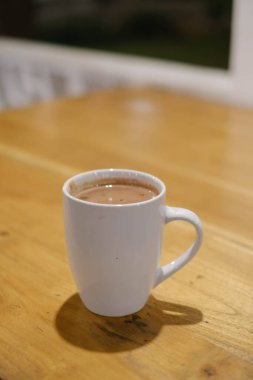 Tablodaki beyaz bardakta bir kahvenin portresi veya dikey ve seçici odak noktası.