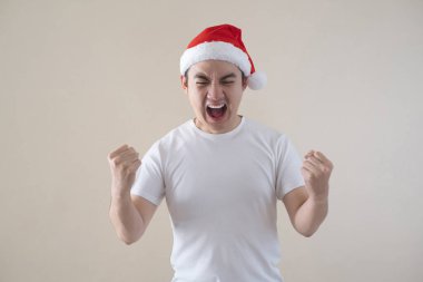 Genç Asyalı Noel Baba heyecanlı ve mutlu bir ifadeyle sağ üst tarafı işaret ediyor. İzole edilmiş bej arka plan. Noel konsepti.