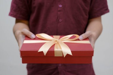 Erkek eller, altın kurdeleyle sarılı küçük kırmızı bir hediye kutusu tutuyor. Yakın çekim ve kapalı çekim. Seçici odaklanma. Noel Konsepti.