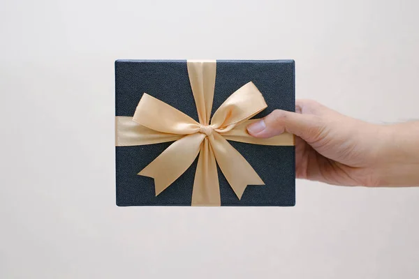 Male hands holding a small blue gift box wrapped with gold ribbon. Isolated white background. Selective focus. Christmas Concept.
