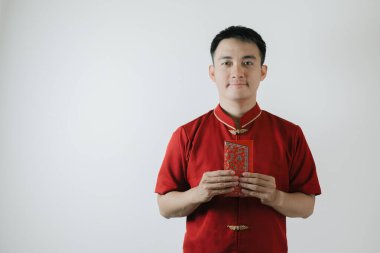 Cheongsam adında geleneksel Çin kumaşı giyen Asyalı bir adam Angpao tutuyor ve beyaz arka plandaki kameraya bakıyor.