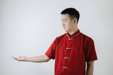 Cheongsam adı verilen geleneksel Çin kumaşı giyen Asyalı adam elini açar ve beyaz arka planda sol tarafa bakar.