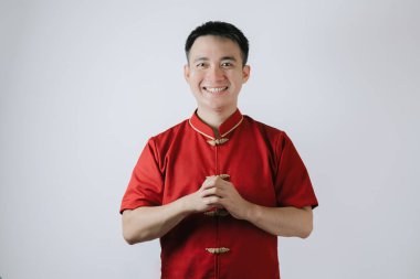 Cheongsam adlı geleneksel Çin kumaşı giyen Asyalı adamın gülümseyen yüzü Ay Yeni Yılı için bir jest yaptı ve beyaz arka plandaki kameraya baktı. Gong Xi Fa Cai.