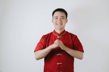 Cheongsam adlı geleneksel Çin kumaşı giyen Asyalı adamın gülümseyen yüzü Ay Yeni Yılı için bir jest yaptı ve beyaz arka plandaki kameraya baktı. Gong Xi Fa Cai.