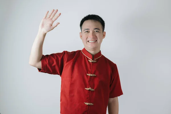 Smile face of Asian man wearing Chinese traditional cloth called Cheongsam is waving hand while looking at the camera on white background. Sign of hi and bye bye.
