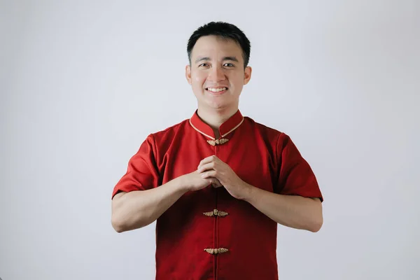 Smile face of Asian man wearing Chinese traditional cloth called Cheongsam with a gesture of congratulations on the Lunar New Year and looking at the camera on white background. Gong Xi Fa Cai.