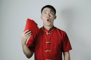 Asyalı bir adamın Cheongsam ya da Çin geleneksel giysilerini giyerken angpao ya da kırmızı para hediyesini beyaz arka planda kullanmasının şok edici yüzü. Gong Xi Fa Cai.