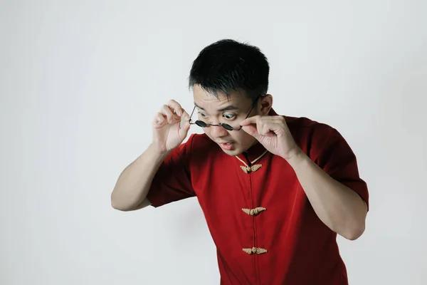 Shocked face of Asian man wearing traditional costume while looking down on white background. Chinese New Year concept. Gong Xi Fa Cai.
