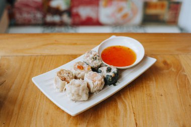 Ahşap masada acı biber soslu bir tabak Dim Sum.