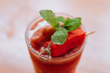 Çilek kokteylinin yakın planında taze taze nane yaprakları ve tahta masaya yerleştirilmiş bir dilim çilek var.