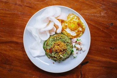 Tahta masada yumurta ve karides krakerleriyle fesleğenli yeşil pilav tabağının düz görüntüsü. Endonezya mutfağı.