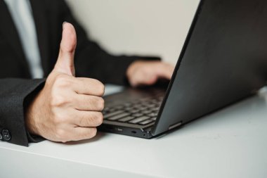 Profesyonel bir adam dizüstü bilgisayar kullanırken kameraya başparmak kaldırıyor. Seçici odak.