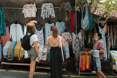 Ubud geleneksel pazarında iki kadın turist yerel satıcıyla pazarlık yapıyordu. Sokak fotoğrafı..