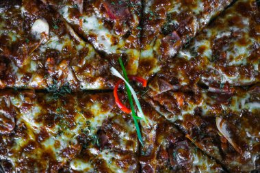 Altın-kahverengi kabuklu ve koyu dokuma yüzeyli pizza, erimiş peynir, tek bir kırmızı biber ve biber sosu, ve bir tutam bitki.