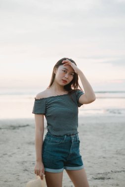 Gün batımında sahilde genç ve güzel bir Asyalı kız Bokeh arka planına sahip kameraya bakarken...