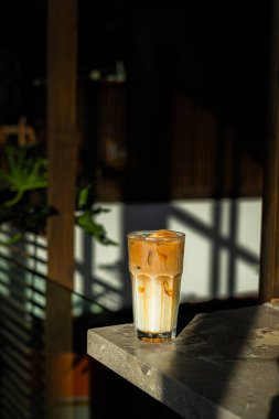 Kahve dükkanında bir bardak buzlu kahve ve sütlü krema. Pencere ve gölgenin kontrastlı güneş ışığı kombinasyonu.