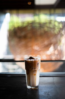 Bir kahve dükkanında, bir bardak buzlu kahve ve sütlü krema. Pencere ve gölgenin kontrastlı güneş ışığı kombinasyonu. Bokeh geçmişi. Dikey veya dikey çekim.