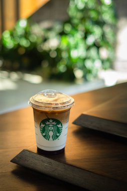 Bokeh arka planlı ahşap bir masada bir fincan Starbucks kahvesi. Dikey veya dikey çekim.