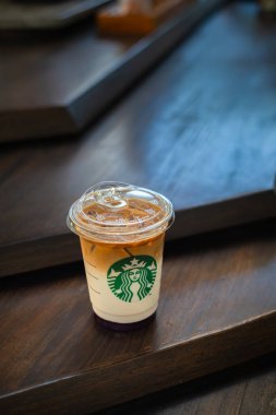 Bokeh arka planlı ahşap bir masada bir fincan Starbucks kahvesi. Dikey veya dikey çekim.