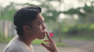 Arka planı bulanık veya bokeh etkisi olan Güneydoğu Asyalı bir adam sigara içiyor. Yavaş çekim görüntüsü.