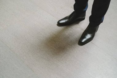Resmi bir pantolon ve beton zeminde duran siyah deri ayakkabılar giyen bir adamın ayakları.