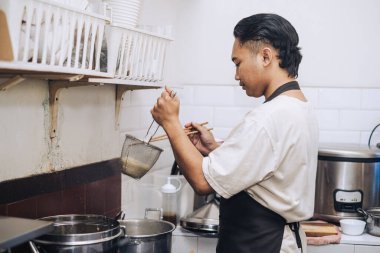 Önlüklü bir Güneydoğu Asyalı şef bokeh arkaplanlı erişte pişiriyor.